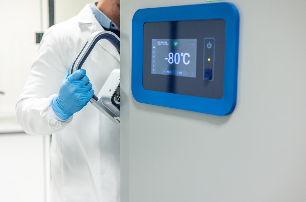 Lab technician in gloves opening a ULT freezer with a door digital display reading -80°C temperature.